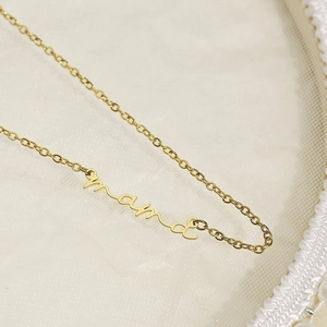 Macro detail of gold 'Mama' script pendant necklace on elegant white lace background