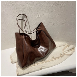 Detail of soft dark brown leather tote bag on a knit sweater showing premium texture