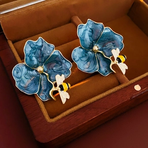 Macro view of vintage blue enamel flower earrings with a small bee detail in jewelry box