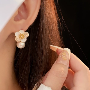 Close-up of floral pearl earrings with white enamel petals and sparkling crystal centers