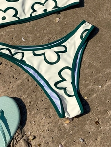 Detail of cream floral bikini set with green contrast trim on sandy beach background