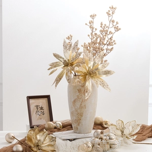 Golden artificial Christmas flowers in a textured vase with decorative ornaments