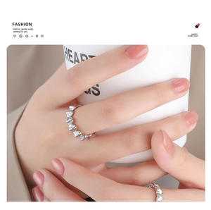 Detail of minimalist silver heart-shaped band rings worn on fingers holding a cup