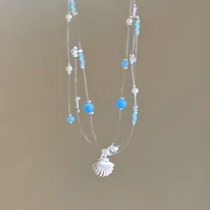 Détail du collier multicouche avec perles bleues, perles blanches et pendentif coquille