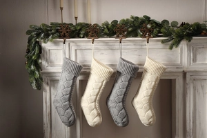 Close-up of four knitted Christmas stockings in grey and ivory on a festive fireplace