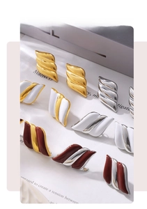 Close-up of geometric 18k gold plated wing studs in multiple colors on a grey background