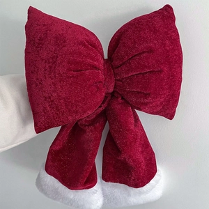 Detailed close-up of large red velvet Christmas bow with white faux fur trim and soft fabric texture
