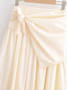 Detailed close-up of cream-colored skirt showing lace trim and side-waist bow tie detail