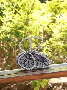 Macro shot of purple butterfly clutch bag featuring rhinestone crystals on a wooden bench