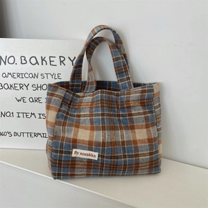 Detail of blue and orange plaid tote bag featuring a stitched brand label and dual handles