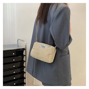 Detail of beige corduroy crossbody bag with gold chain strap shown on a model