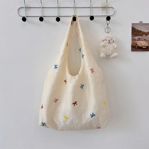 Close-up of embroidered bow detail on cream-white shoulder bag hanging in a cozy setting