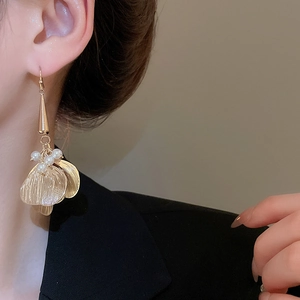 Close-up of golden hollow petal earrings with pearl tassels worn on a model ear