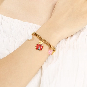 Detail of gold chain bracelet featuring colorful ladybug and heart charms on wrist