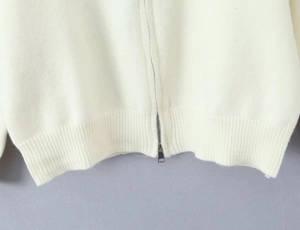 Detailed shot of white knit cardigan with silver zipper and ribbed hem texture