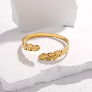 Detailansicht eines goldenen Armreifs in Federform auf einem weißen strukturierten Stein