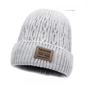 Detail of light gray cable knit beanie featuring a brown faux leather fashion label