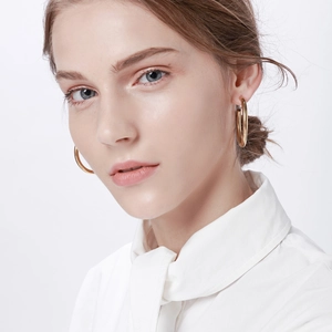 Close-up of large polished gold C-shape hoop earrings on a model in a white shirt