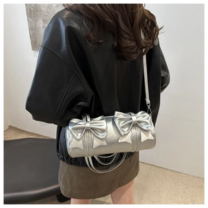Detail of silver cylinder bag with decorative double bows and slim crossbody strap