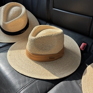 Close-up of handmade raffia fedora hats with brown and black bands on leather
