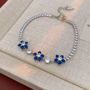 Detailed view of silver flower bracelet with blue and white zircons on linen jewelry box