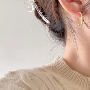 Close-up of elegant gold twisted hoop earring worn by a model in a minimal setting