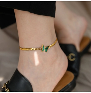Detail of a 18K gold plated anklet with a green enamel butterfly on a woman's ankle