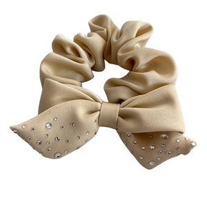 Beige satin scrunchie with bow and scattered rhinestones on white background