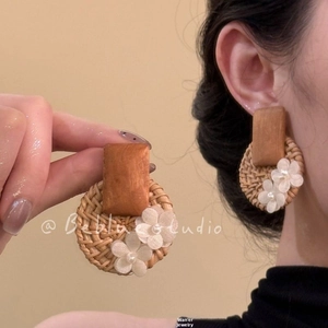 Gros plan de boucles d'oreilles bohèmes avec rotin tressé, bois et fleurs en tissu