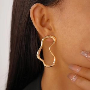 Detail of a minimalist gold irregular geometric earring worn by a female model