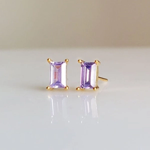 Macro shot of emerald-cut purple zircon stud earring with classic gold four-prong setting