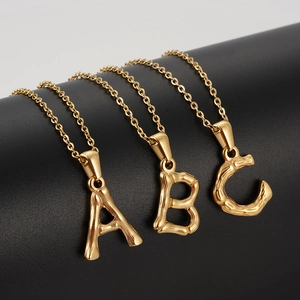 Close-up of golden bamboo textured alphabet pendants A B C in polished stainless steel