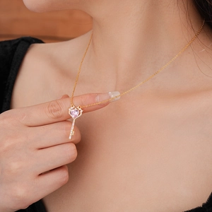 Detail of a gold key pendant necklace featuring a pink heart zircon on a model