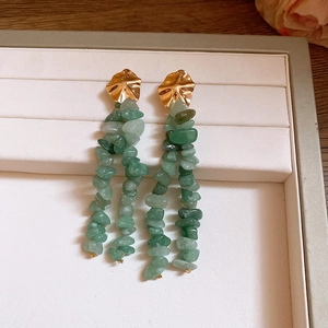 Eleganti orecchini a fiore dorati con nappe in pietra verde in una scatola per gioielli