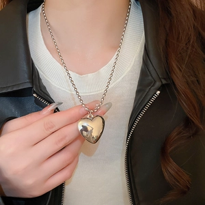 Close-up of a large polished silver heart pendant necklace on a bead chain with a mirror finish