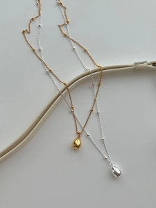 Detailed view of minimalist teardrop pendants in gold and silver with delicate beaded chains