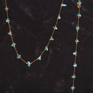 Macro view of 18K gold-plated stainless steel chain with turquoise stones on dark background