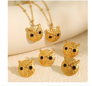 Detailed view of gold owl jewelry set with black diamond eyes on beige background