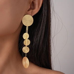 Detail of long gold tassel earrings with textured circular disks on a model