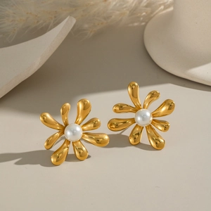 Close-up of elegant gold flower earrings with white pearl centers on a beige background