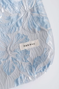 Macro view of blue lily floral jacquard fabric texture and H & R BAG woven label
