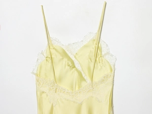 Dettaglio di un top in raso giallo brillante con pizzo bianco e spalline sottili