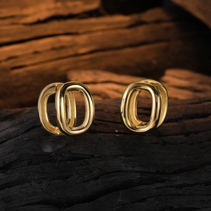 Detailed close-up of golden U-shaped oval hoop earrings on a dark textured wood background