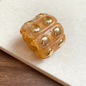 Macro shot of amber resin bracelet with gold studs on a warm minimalist background