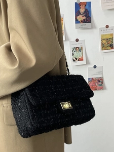 Detail of black tweed crossbody bag with gold buckle and metallic chain strap