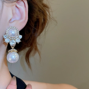 Close-up of a gold pearl pendant earring with sparkling zircons on a model's ear