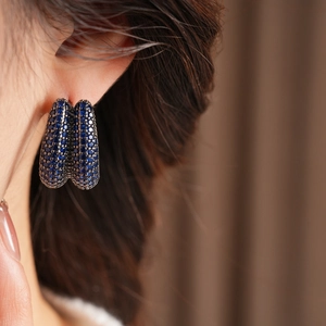 Close-up of vintage U-shaped earrings featuring deep blue zircon stones on a model ear
