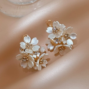 Floral C-shape earrings with white acrylic petals and crystals on champagne silk background