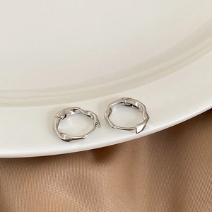 Detailed view of silver twisted wave hoop earrings on a ceramic tray with silk