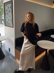 Schickes schwarzes Oversized T-Shirt kombiniert mit einem weißen Satin-Midirock im Café